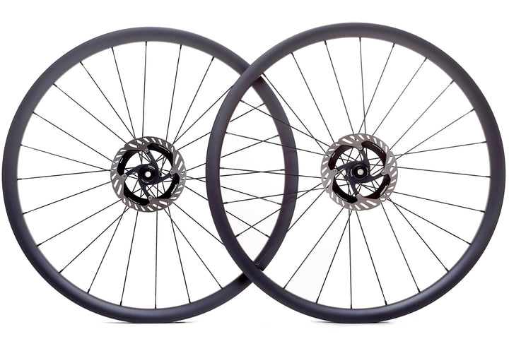 Par de ruedas de carbono 30mm para gravel, perfil aerodinámico, bujes Ratchet System y diseño Tubeless Ready, ideales para estabilidad y rendimiento en terrenos mixtos.